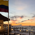 Beachside restaurant with tables and chairs under a colorful sunset sky.