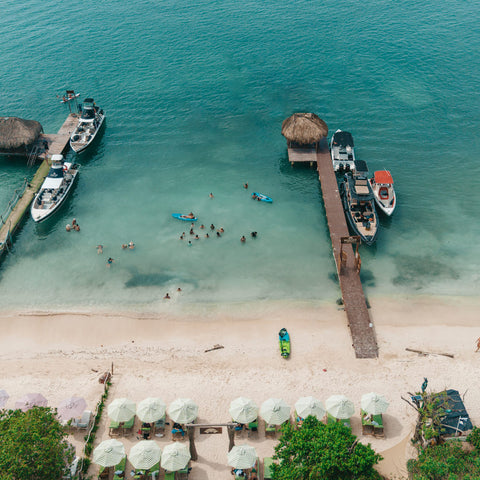 Aerial view of a tropical beach with people, boats, and umbrellas.